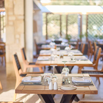 Cozy indoor steakhouse dining area with wooden tables, black woven chairs, and soft natural lighting.