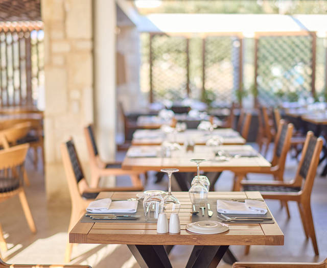 Cozy indoor steakhouse dining area with wooden tables, black woven chairs, and soft natural lighting.