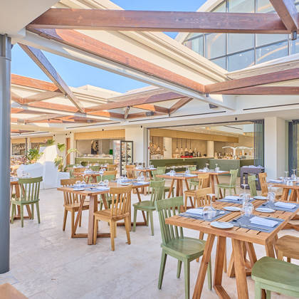 Stylish semi-outdoor dining area with green and wooden chairs, open kitchen, and retractable roof under natural light