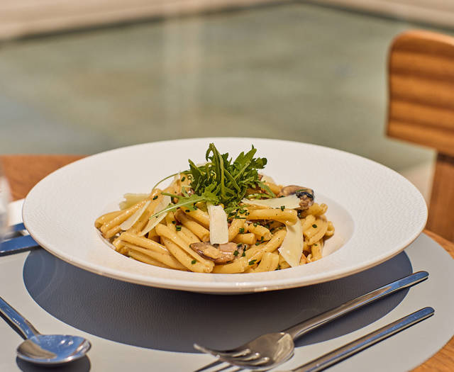 Creamy pasta with mushrooms, shaved cheese, and fresh greens served in an outdoor dining setting.