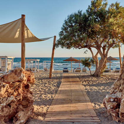 Beach pathway between two rocks with sunbeds under wooden canopies