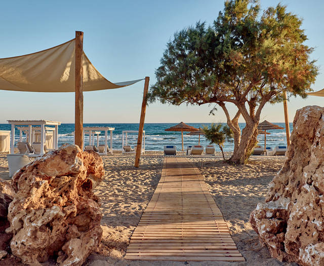 Beach pathway between two rocks with sunbeds under wooden canopies