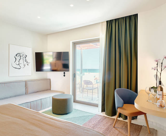Bright junior suite with double bed, sofa, modern wooden desk and access to a private balcony