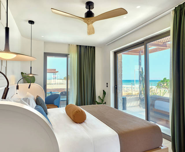 Bright bedroom with double bed, ceiling fan, and sliding glass doors opening to sea-facing patio.