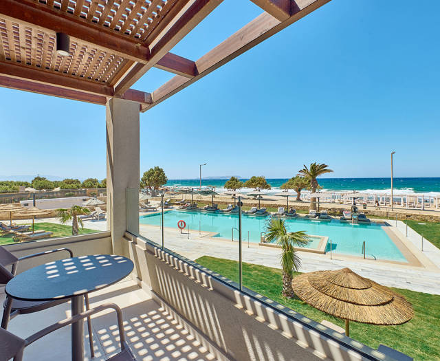 Double room's shaded balcony with seating and panoramic view of the pool area and the sea beyond.