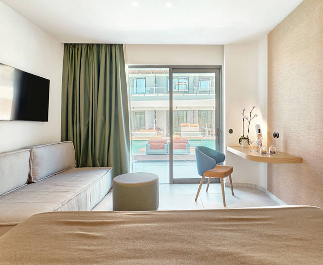 Swim-up junior suite interior with double bed, sofa, desk and direct access to the pool through sliding doors.