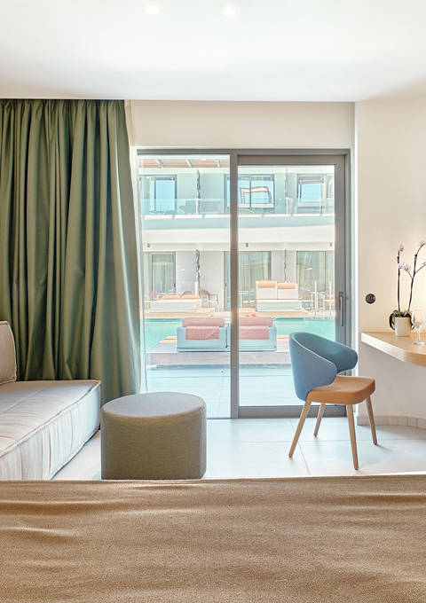 Swim-up junior suite interior with double bed, sofa, desk and direct access to the pool through sliding doors.