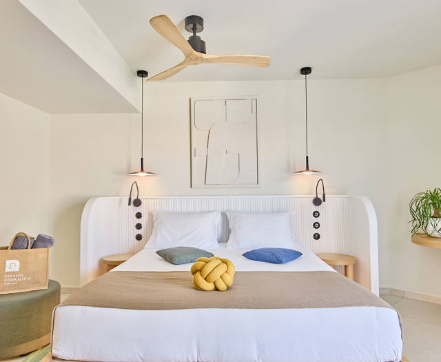Double bed with pendant lighting, ceiling fan, and a corner desk in a suite with side sea view