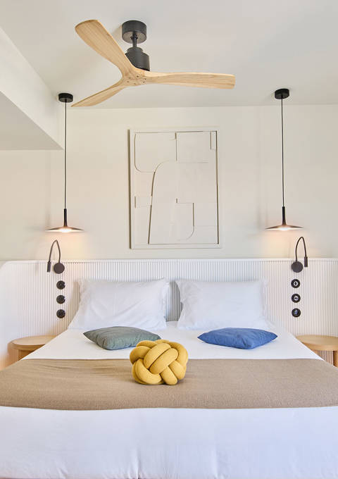 Double bed with pendant lighting, ceiling fan, and a corner desk in a suite with side sea view