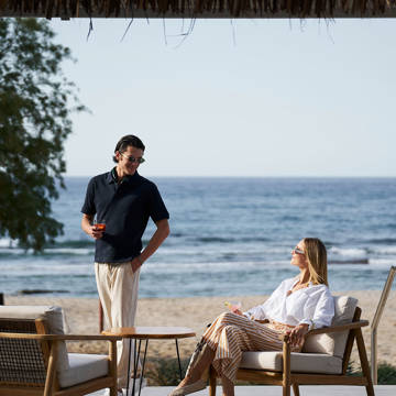 Couple enjoying drinks by the beach on outdoor lounge chairs.