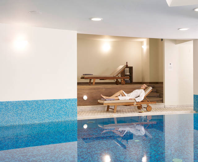 Guest relaxing on a lounger beside the indoor pool in the spa area