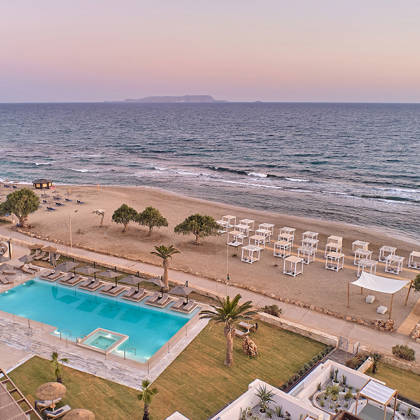 Aerial view of beachfront pool and private loungers on the sand at Kosta Alimia during sunset.