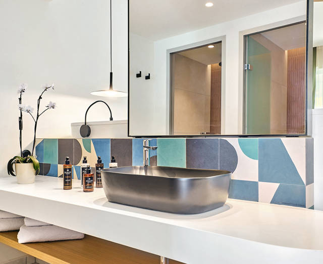 Modern bathroom with black sink, geometric tile backsplash, large mirror, and built-in wooden shelves.