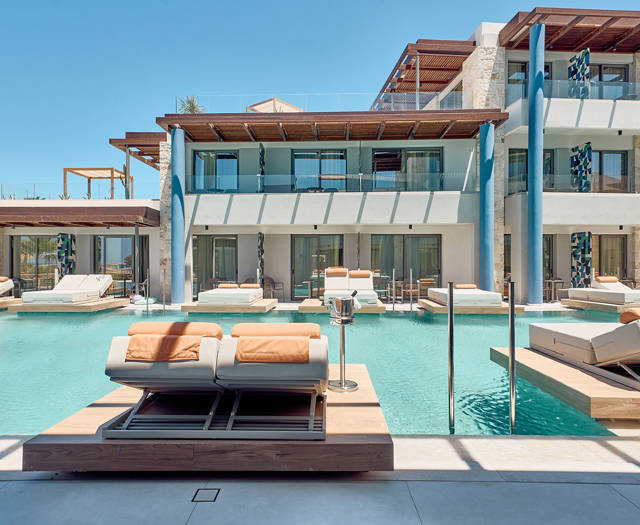 Swim-up rooms with sun loungers on private decks, surrounding a shared pool with a view of the sea.