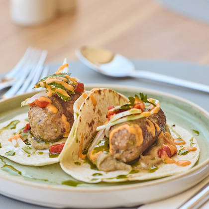 Gourmet meat tacos topped with diced vegetables and sauce, served on a ceramic plate.