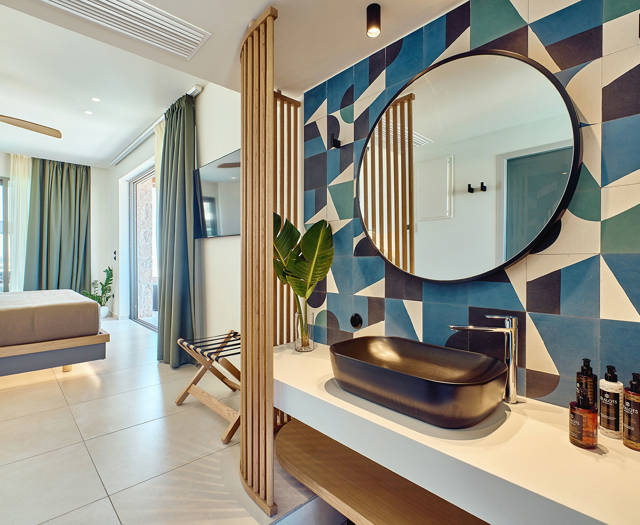 Retreat double room with open-plan bathroom featuring a round mirror, patterned tile wall, and black basin, adjacent to a minimalist bedroom area.