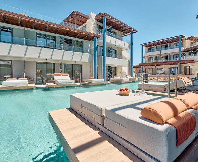 Luxurious swim-up terrace with double sunbed on floating deck, facing shared pool and sea-view suites.