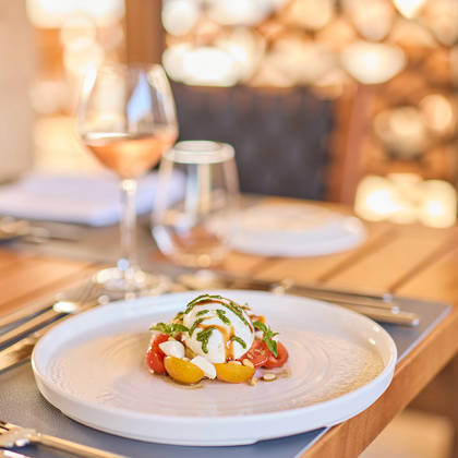 Caprese-style dish with mozzarella and cherry tomatoes, served on a set table with a glass of rosé wine.