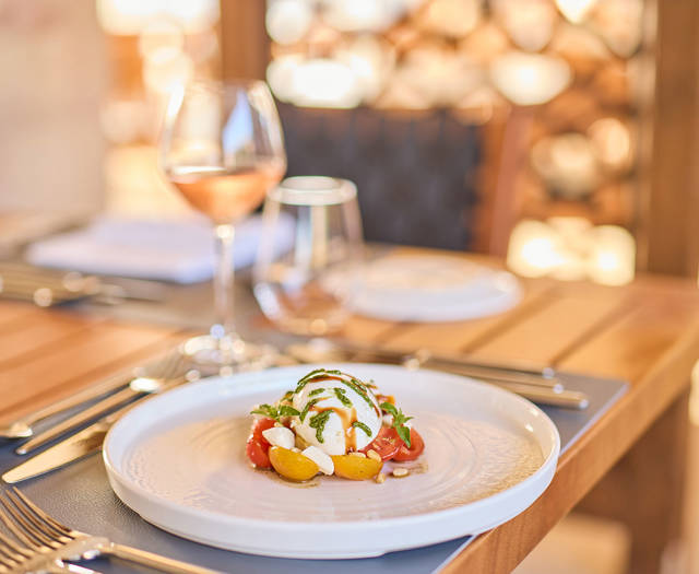 Caprese-style dish with mozzarella and cherry tomatoes, served on a set table with a glass of rosé wine.