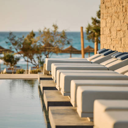Row of sun loungers by a pool at Kosta Alimia, with a view of the sea in the background