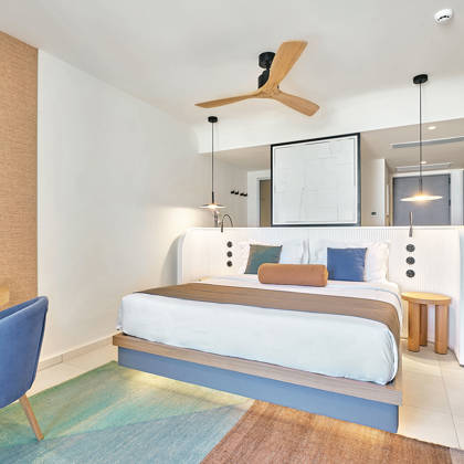 Bright junior suite with double bed, blue chair and a desk, and colorful area rug.