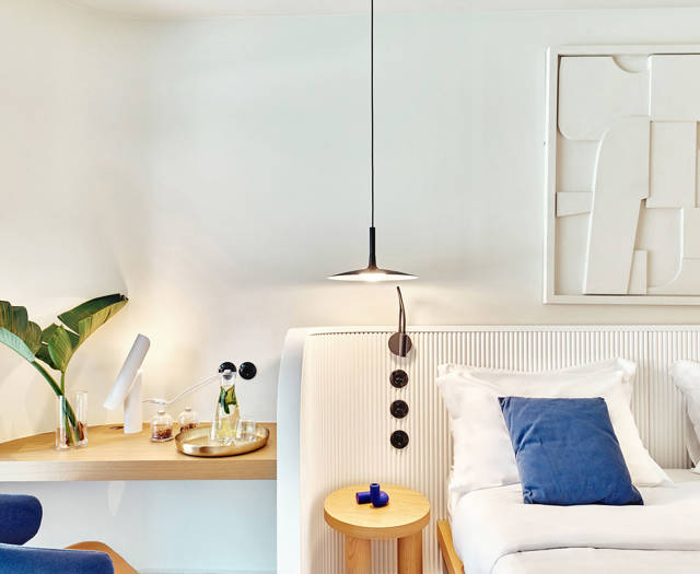 Elegant corner of a swim-up room with bed, bedside table, hanging light, and a desk with welcome drinks.