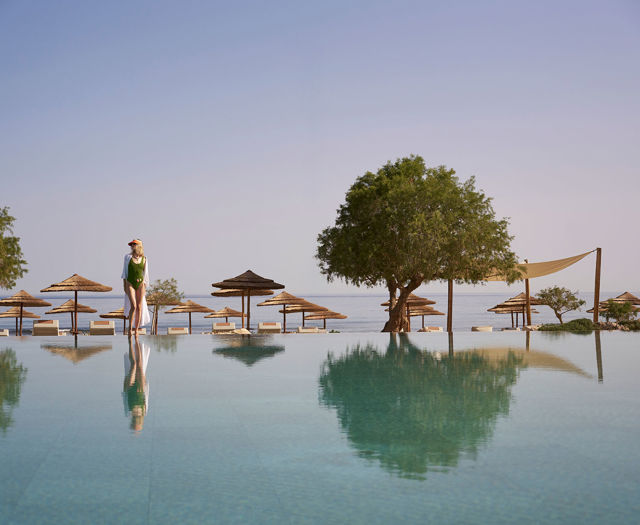 Woman standing near an infinity pool with a view of the sea and beach umbrellas