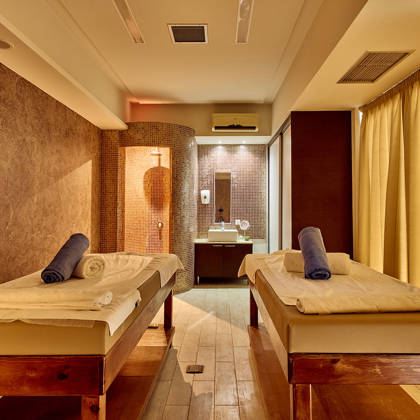 Warmly lit spa treatment room with two massage tables and a private shower area.