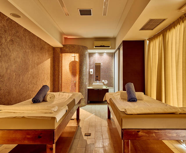 Warmly lit spa treatment room with two massage tables and a private shower area.