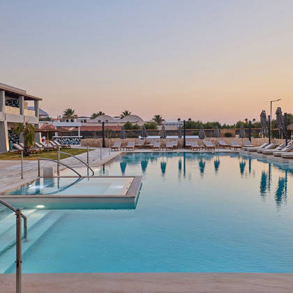Outdoor pool surrounded by lounge chairs at sunset