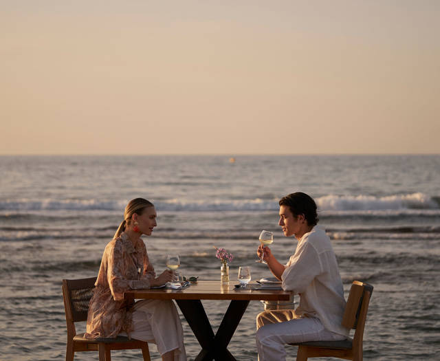 Couple dining at a table by the sea during sunset.