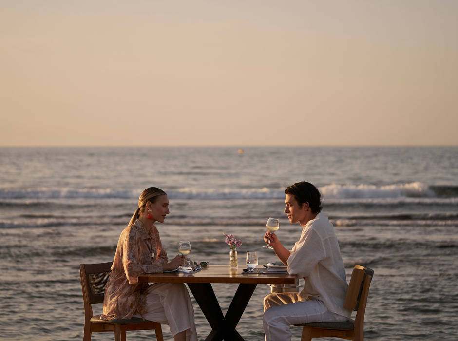 Couple dining at a table by the sea during sunset.