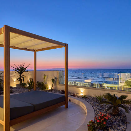 Canopy bed overlooking the sea at sunset, with garden lighting and coastal views at Kosta Alimia.
