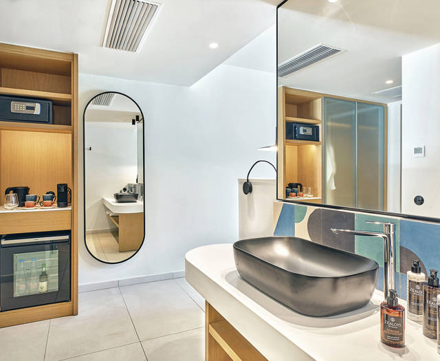 Modern bathroom with black sink, geometric tile backsplash, large mirror, minibar, and built-in wooden shelves.