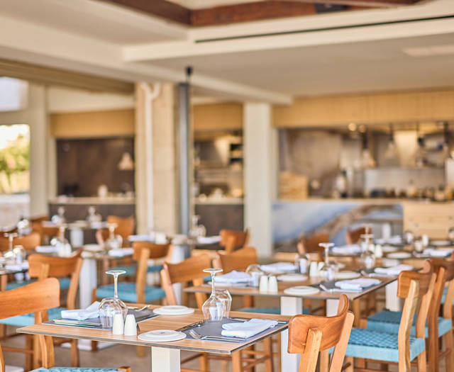 Coastal-style seafood restaurant with neatly set wooden tables and an open kitchen in the background.