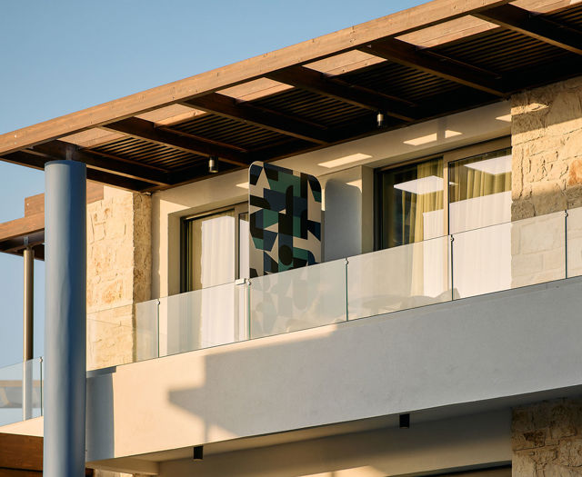 Close-up of a balcony with glass railing, stone wall details, and geometric privacy panel