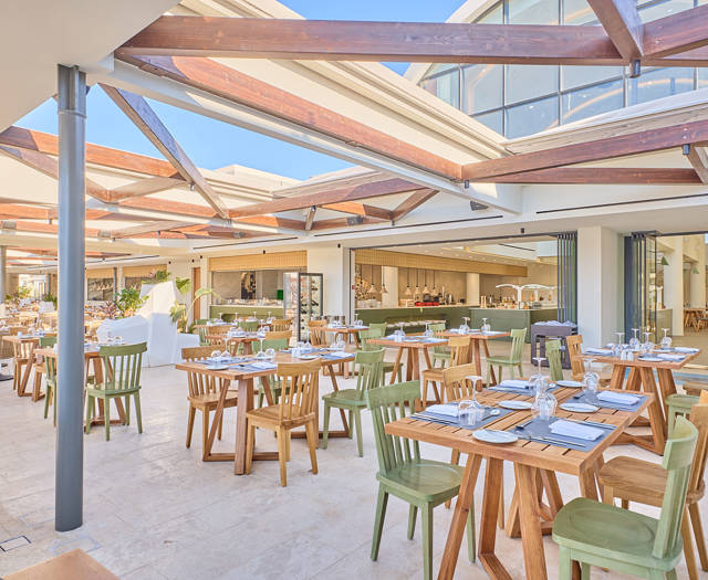 Stylish semi-outdoor dining area with green and wooden chairs, open kitchen, and retractable roof under natural light