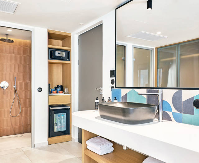 Stylish rooftop room's bathroom with walk-in shower, open shelving, and large mirror above a designer sink.