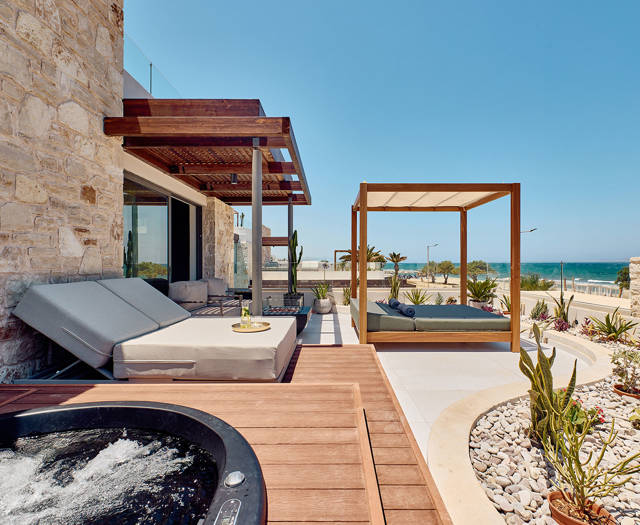 Outdoor terrace with sunbeds, a canopy daybed, a hot tub, and a sea view beyond desert landscaping.