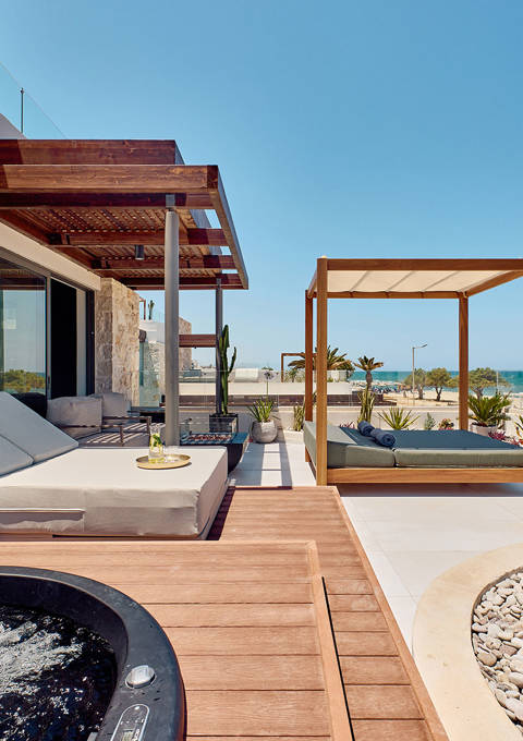 Outdoor terrace with sunbeds, a canopy daybed, a hot tub, and a sea view beyond desert landscaping.