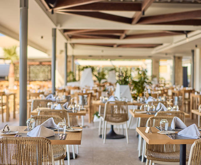 Spacious open-air dining area with neatly arranged wooden tables, wicker chairs, and natural lighting.