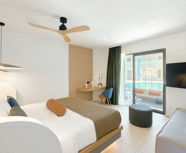 Junior suite with double bed, a desk with a blue chair, a sofa, a wall mount TV and direct access to the pool