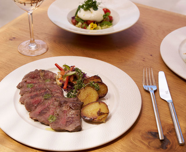 Sliced grilled steak with roasted potatoes and vegetables on a white plate.