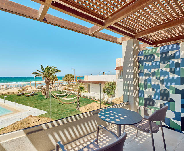 Double room's balcony with table and chairs overlooking the pool, palm trees, and the sea.