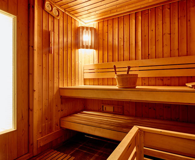 Warm wooden sauna interior with benches, soft lighting, and a water bucket.