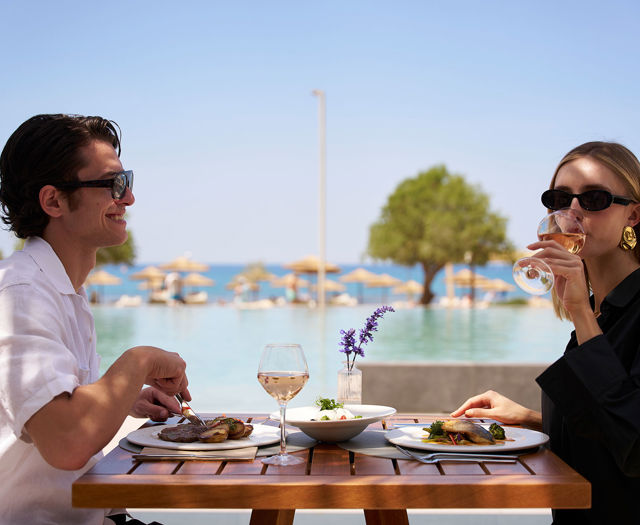 Couple enjoying a meal with wine at an outdoor restaurant table by the pool