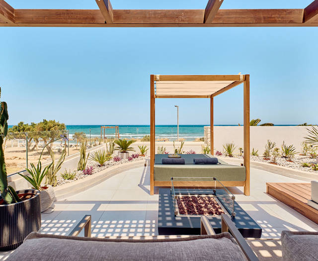 Private terrace with canopy daybed, lounge chairs, and sea view under a wooden pergola.