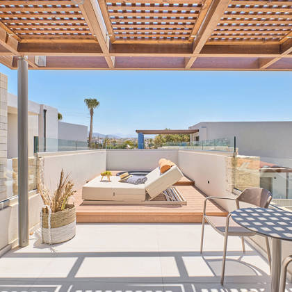 Shaded rooftop lounge with dining table, sun loungers, and views over the resort.