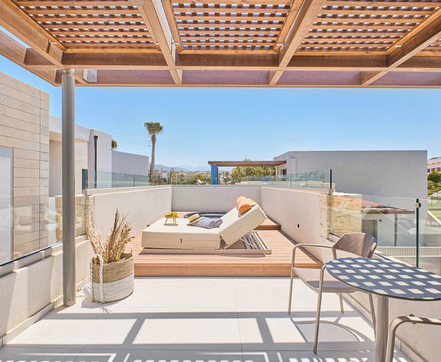 Shaded rooftop lounge with dining table, sun loungers, and views over the resort.