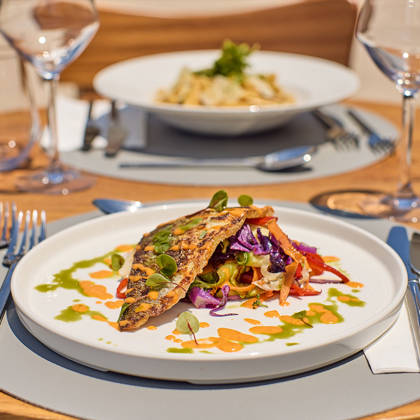 Grilled fish fillet served with colorful vegetables and artistic sauce presentation on a sunlit outdoor table